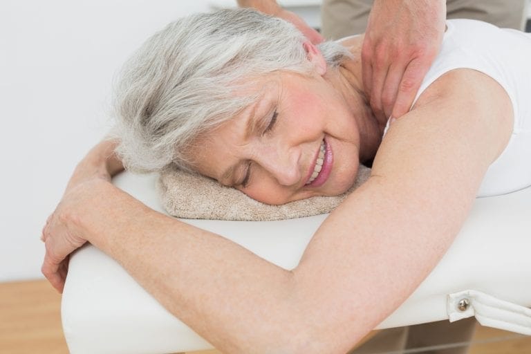 Male physiotherapist massaging a senior woman's shoulder in the