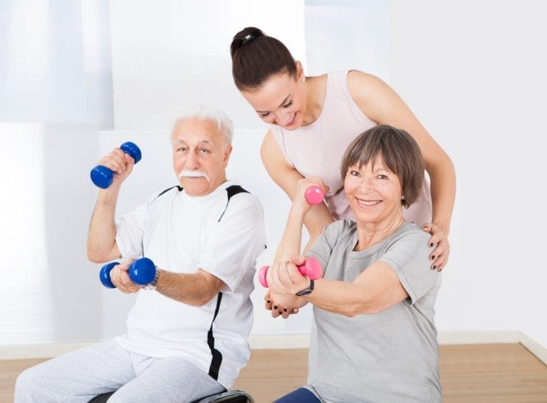 Trainer Assisting Senior Couple With Dumbbells