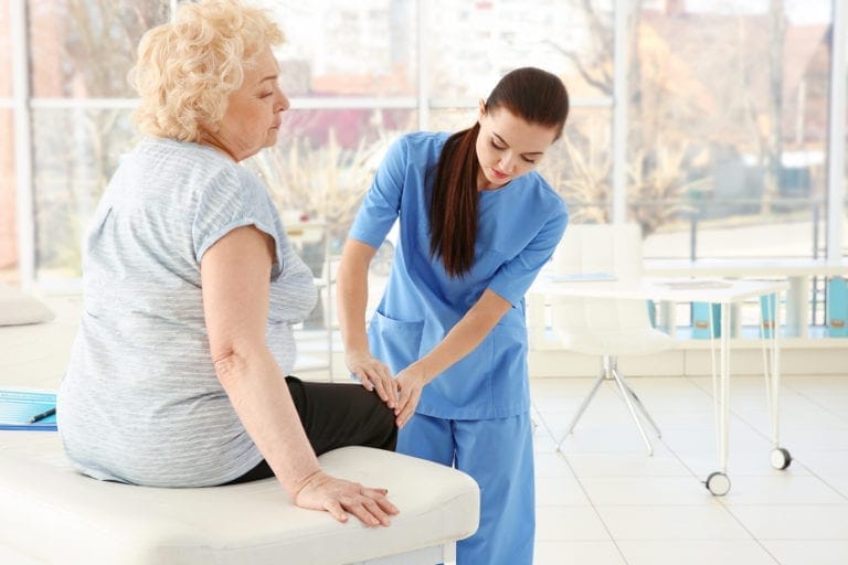 A physical therapist providing knee pain relief to a senior woman