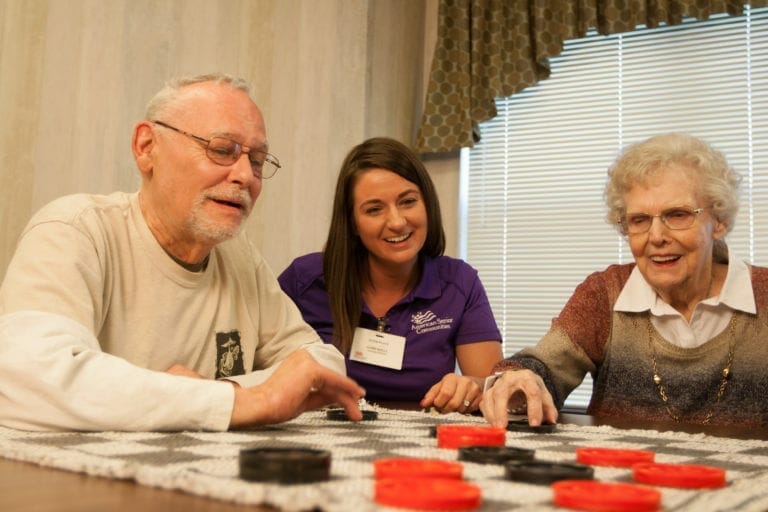 Allisonville Meadows Assisted Living residents and memory care aide playing checkers.