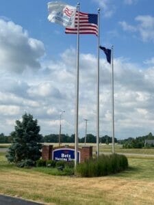 Betz Nursing Home front sign made of brick with blue paneling with white letters. Three flag poles showing the American Senior Communities, American, and Indiana state flags stand next to it.