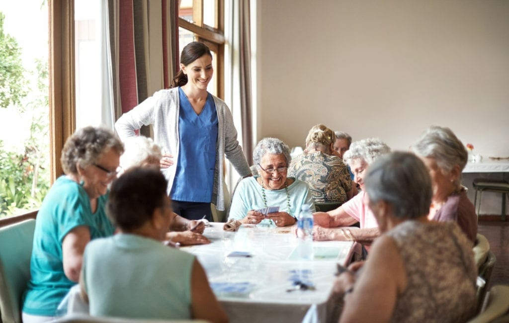 Group of respite seniors playing a board game while a nurse supervises.