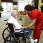 CNA speaking with senior woman in a wheelchair and holding her hand.