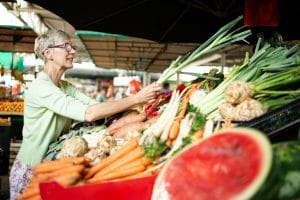 Elderly woman choosing and buying healthy vegetables in farmers' market.