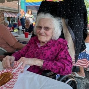 Centenarian Opal Masters sitting in chair outside in a pink and purple blouse