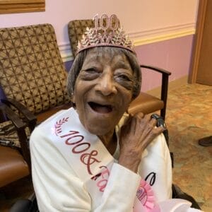 Centenarian Catherine Conn with pink crown that says "100" and white sash with shiny pink lettering that says "100 and Fabulous"