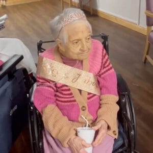 Centenarian Margaret Finney in pink sweater with gold sash and pink tiara