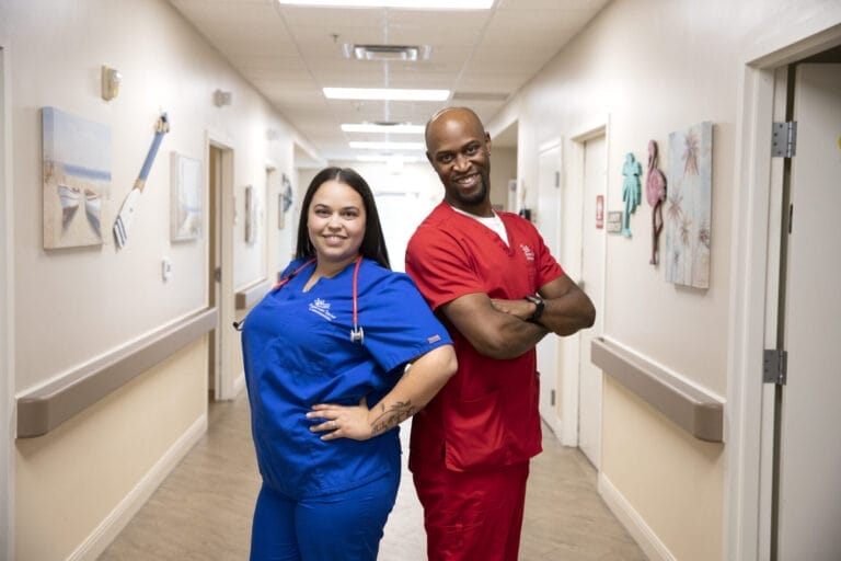 A nurse and CNA standing back to back.