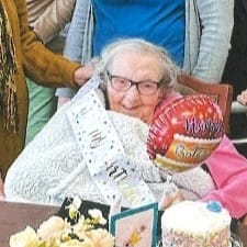 ASC Centenarian Edna Bonnell wearing a pink sweater with a white and gold sash that reads 'It's my birthday" while holding a mini birthday balloon