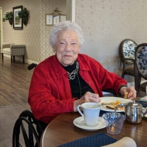 Centenarian Betty Wolf enjoying breakfast while wearing a lovely black blouse, a silver necklace and earrings and red cardigan