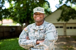 African American Sergeant U.S. Army standing arms crossed in front of residential home and smiling.