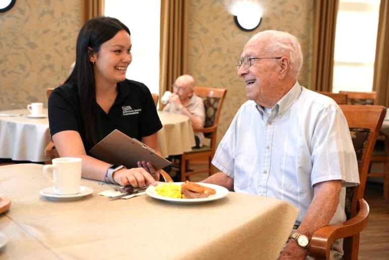 Nutricionista hablando con el residente en la mesa con un plato de comida delante del residente.